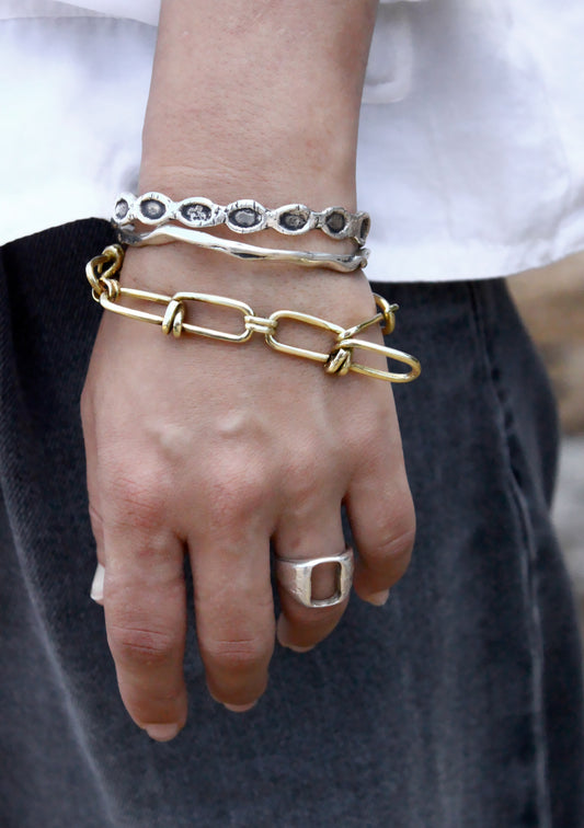 Hand wearing multiple bracelets and a ring on a neutral background