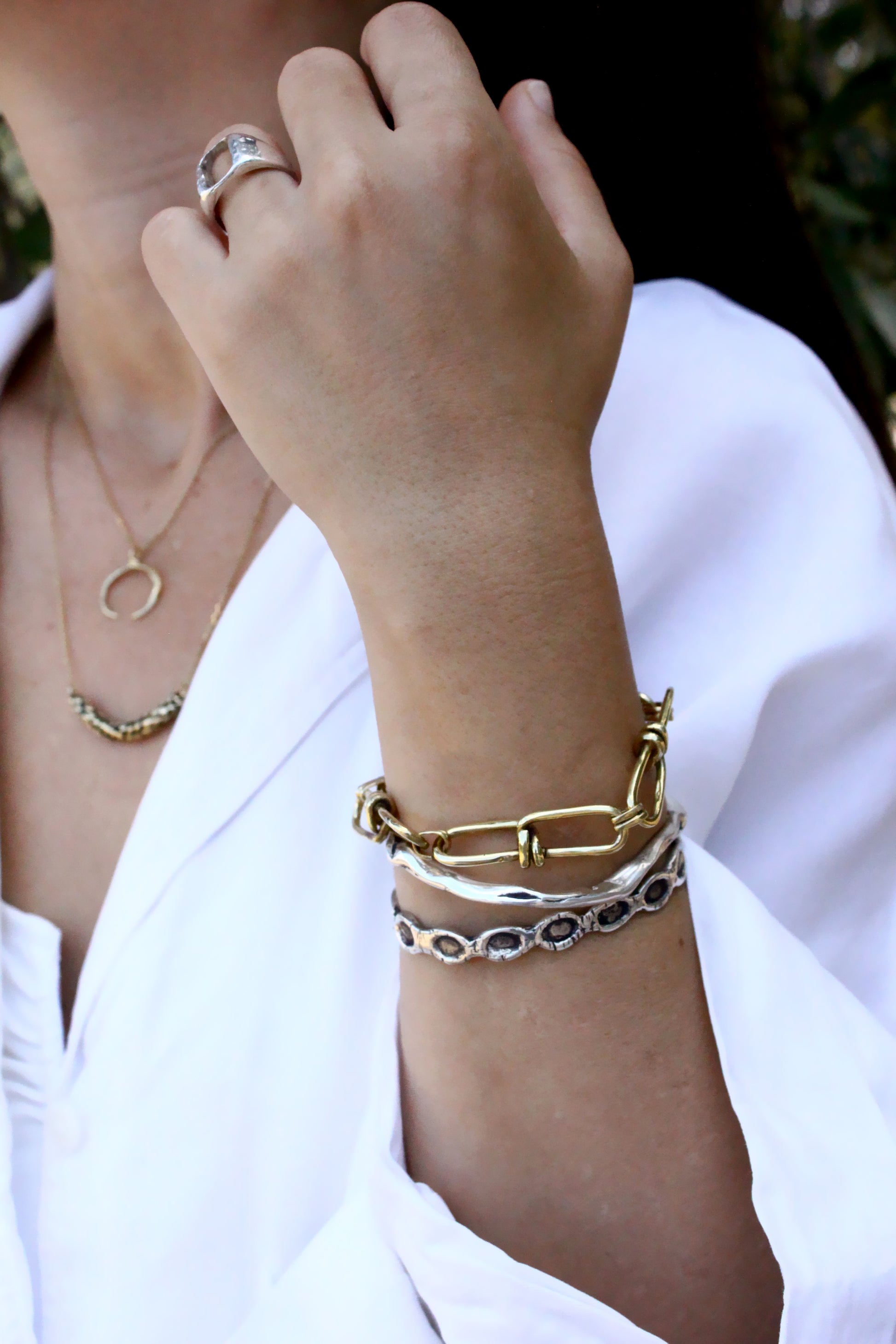 Close-up of a person's wrist with gold bracelets and rings, wearing a white shirt.