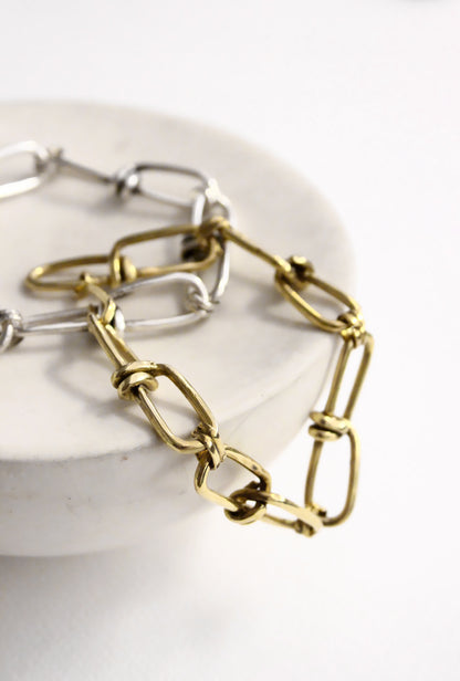 Two chain bracelets, one gold and one silver, on a white plate.