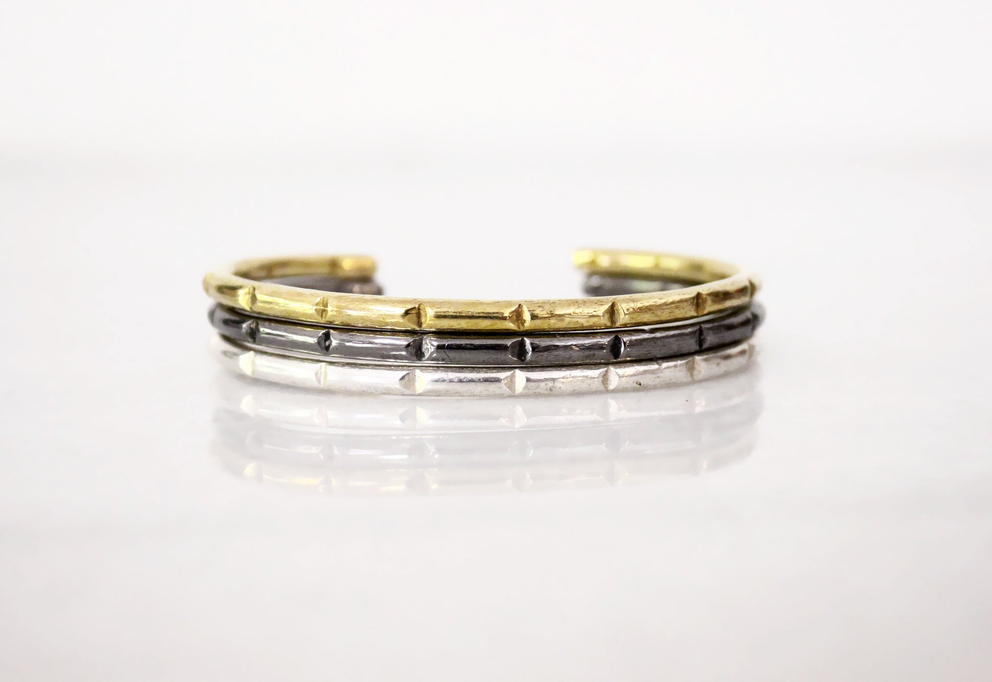 Three-layered bracelet with gold, silver, and black minimal bar cuffs
