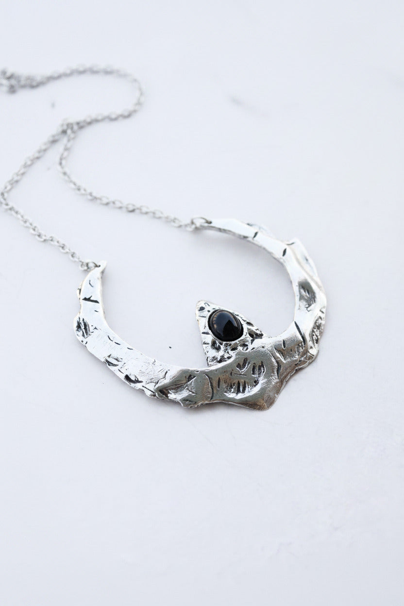 Silver necklace with a black stone on a light gray background