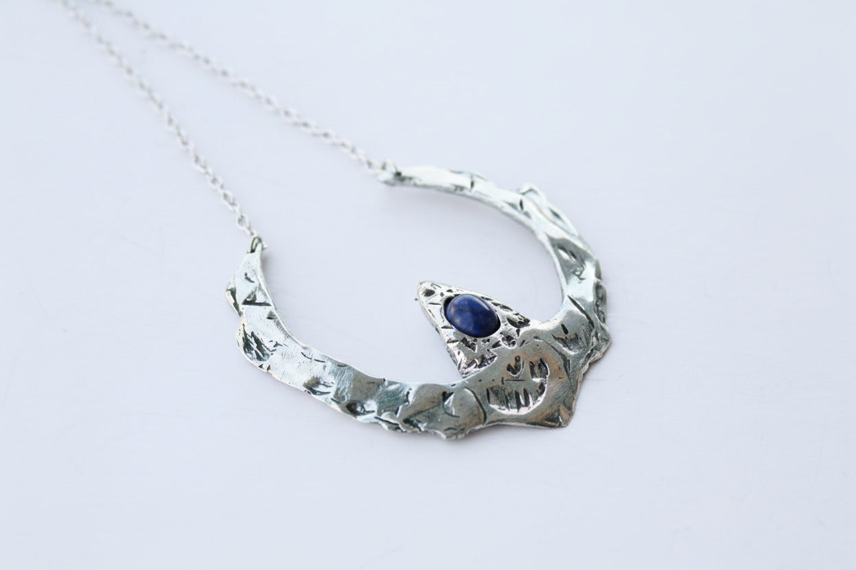 Silver necklace with a blue gemstone on a light gray background