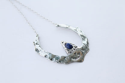 Silver necklace with a blue gemstone on a light gray background