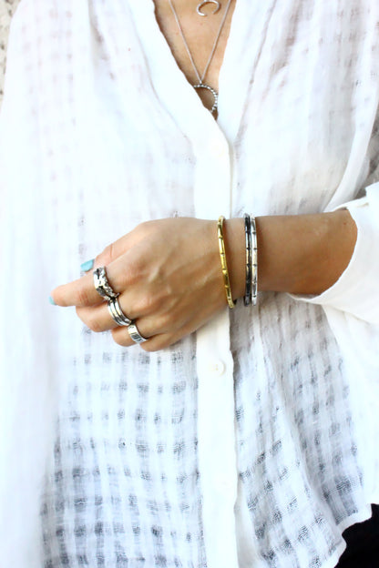 Close-up of a person's hand wearing multiple bracelets and rings with a white shirt in the background.