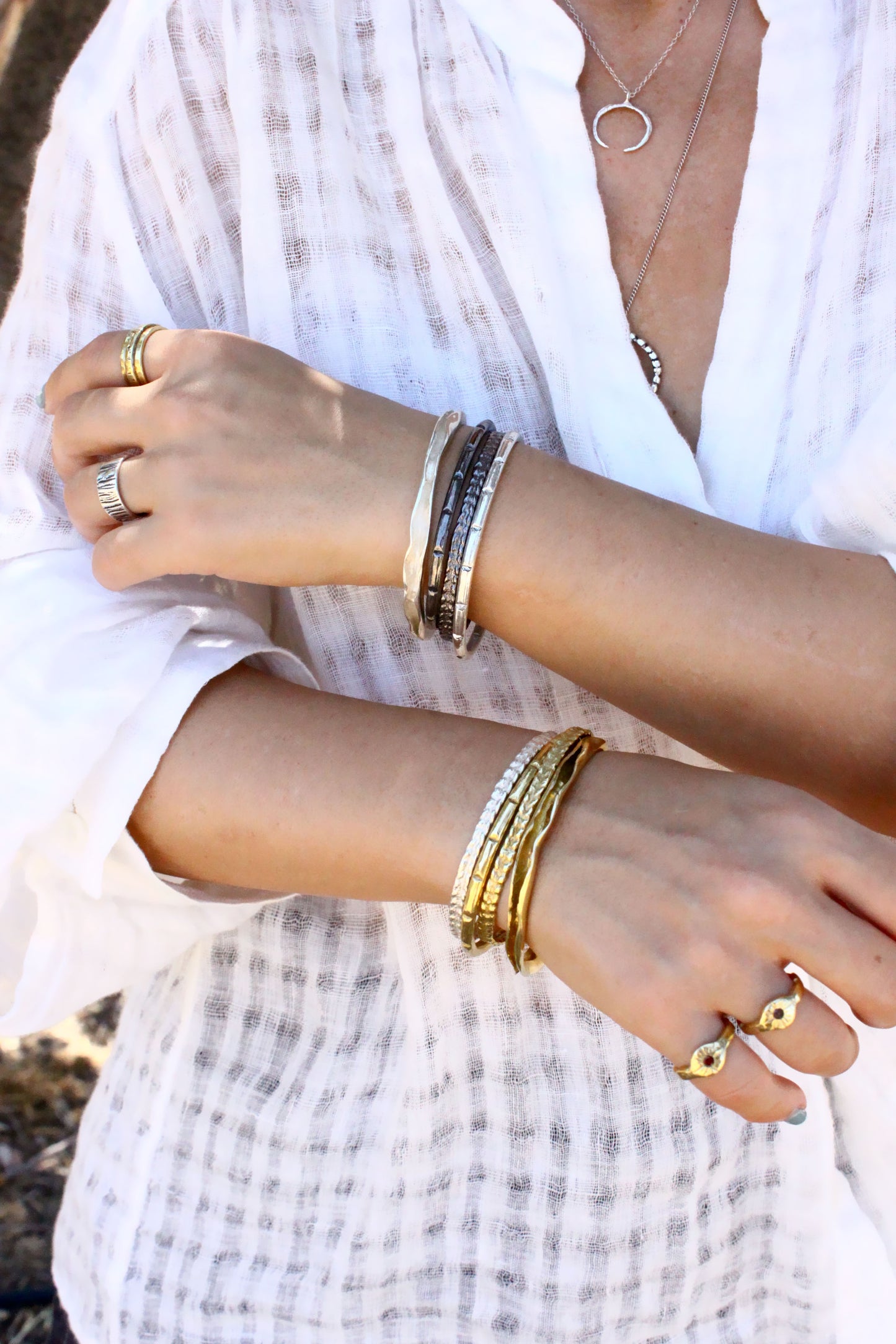 Close-up of a person's arms wearing multiple bracelets and rings with a blurred background.