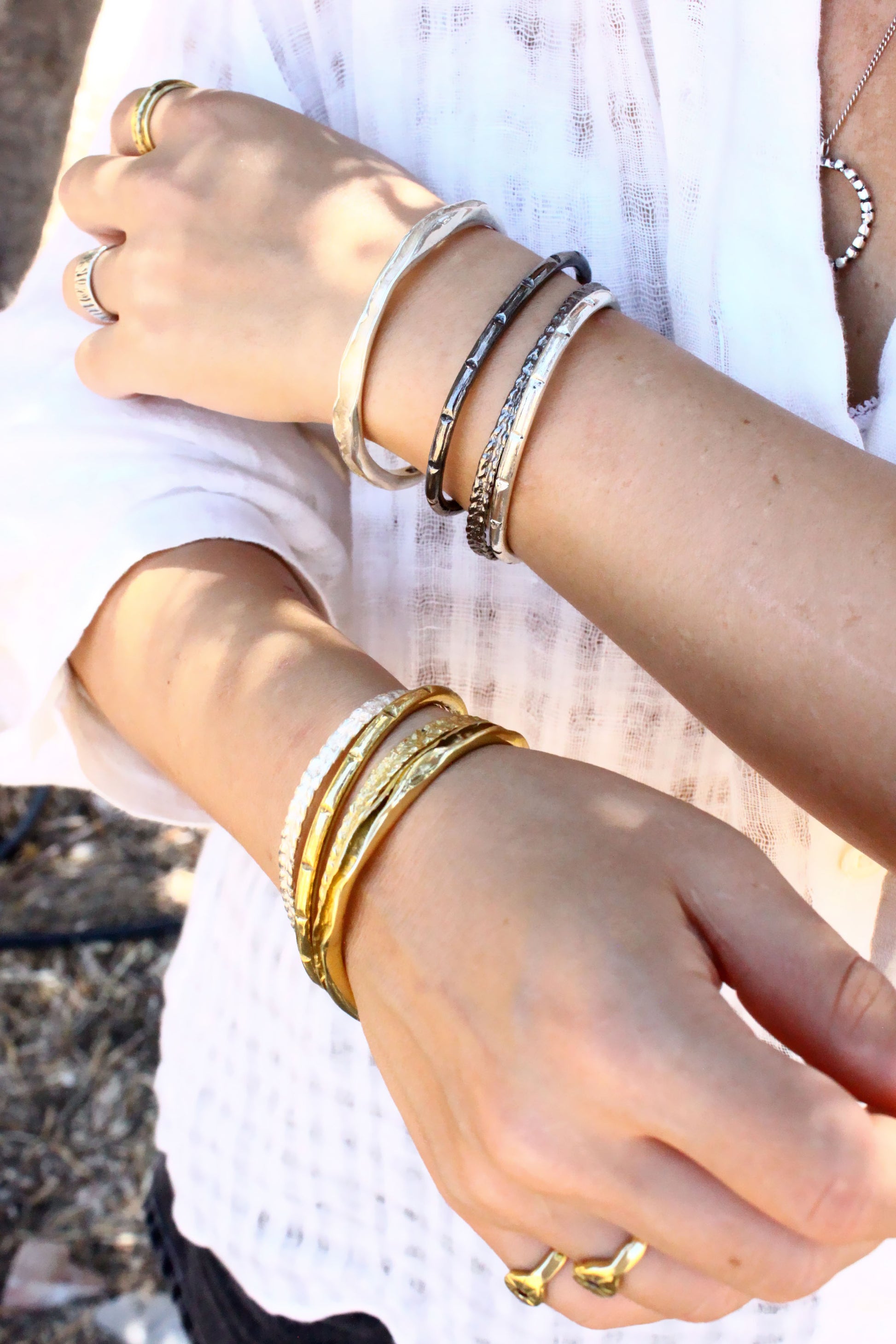 Close-up of hands wearing multiple gold bracelets on a blurred natural background