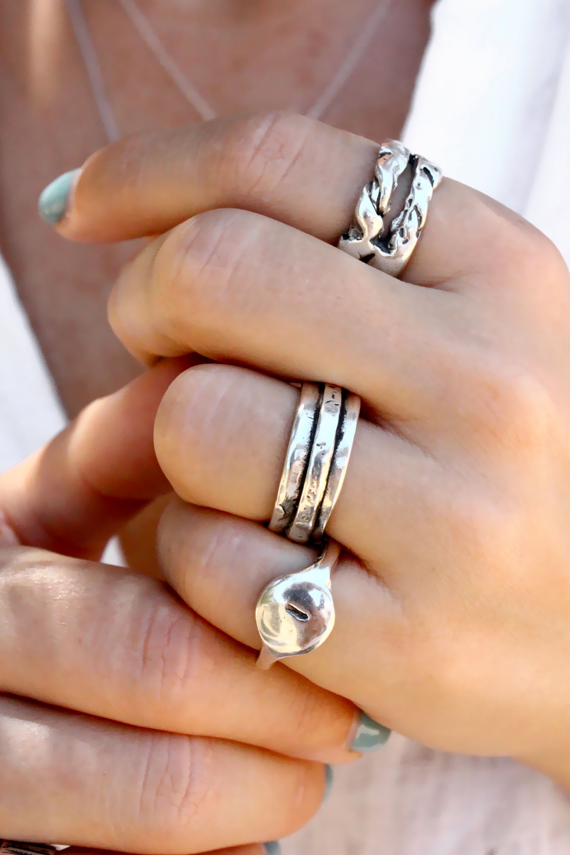 Close-up of a hand wearing multiple silver rings with a blurred background