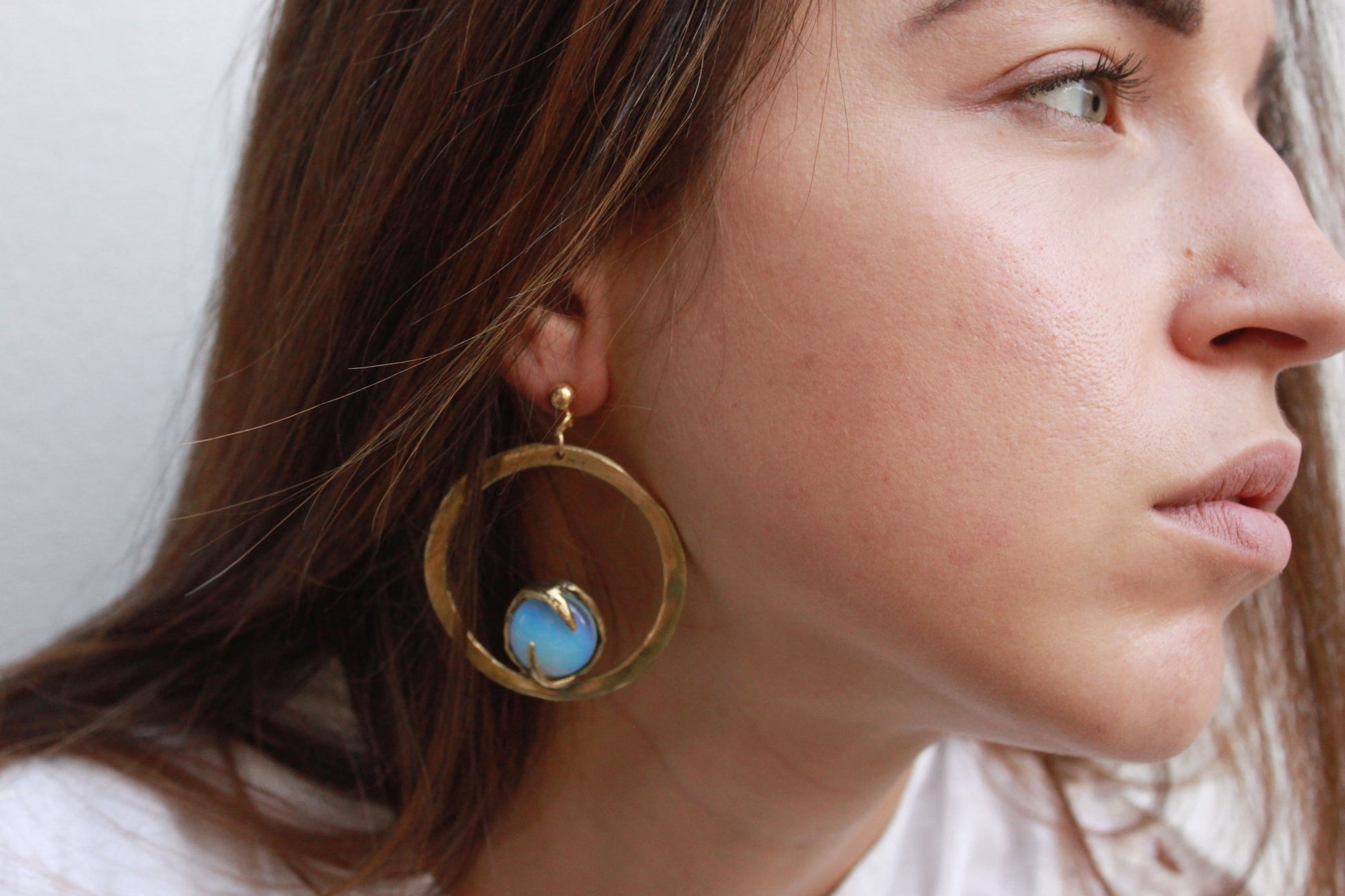 Close-up of a woman wearing gold earrings with a blue gemstone.