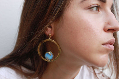 Close-up of a woman wearing gold earrings with a blue gemstone.