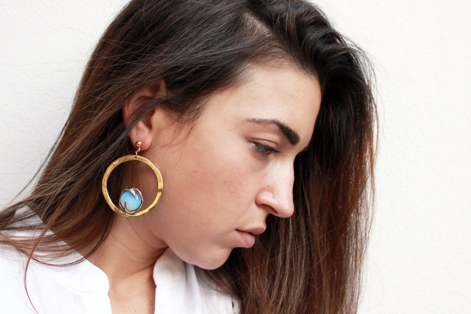 Woman wearing a gold hoop earring with a blue gemstone on a white background
