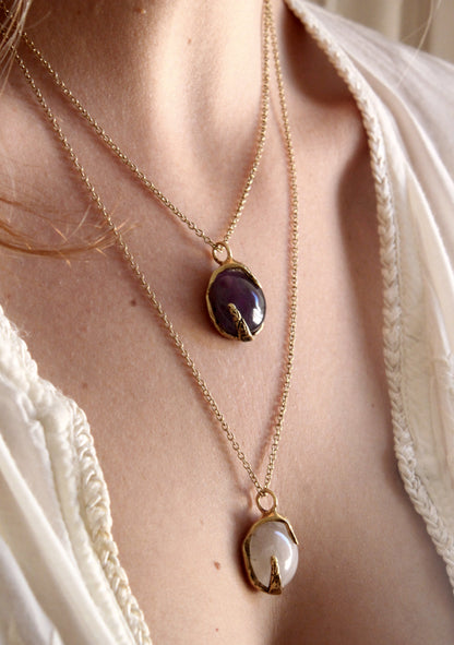 Two gold necklaces with purple and clear stone pendants