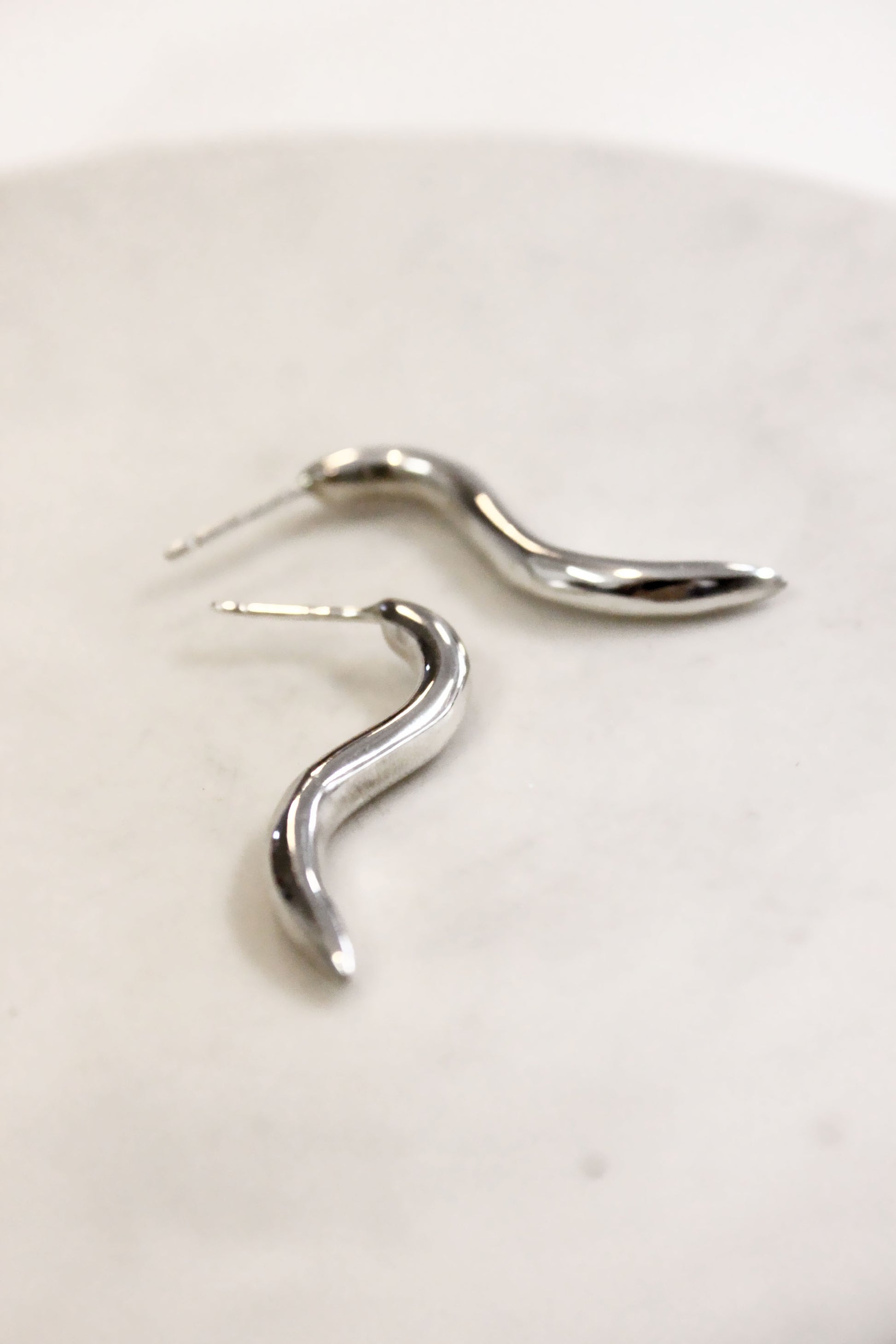 Silver wavy earring on a light beige background