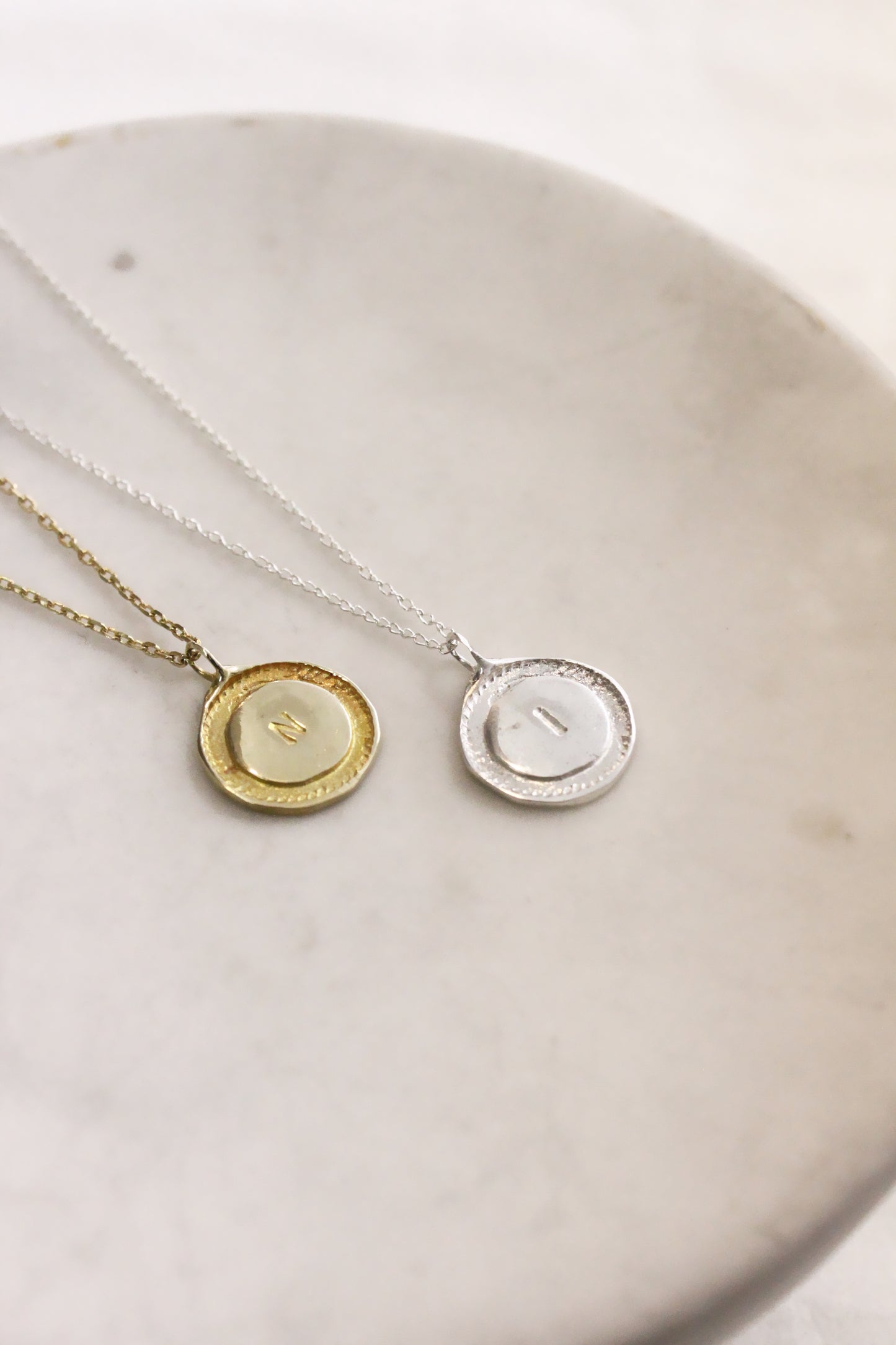 Two necklaces with circular pendants on a white dish