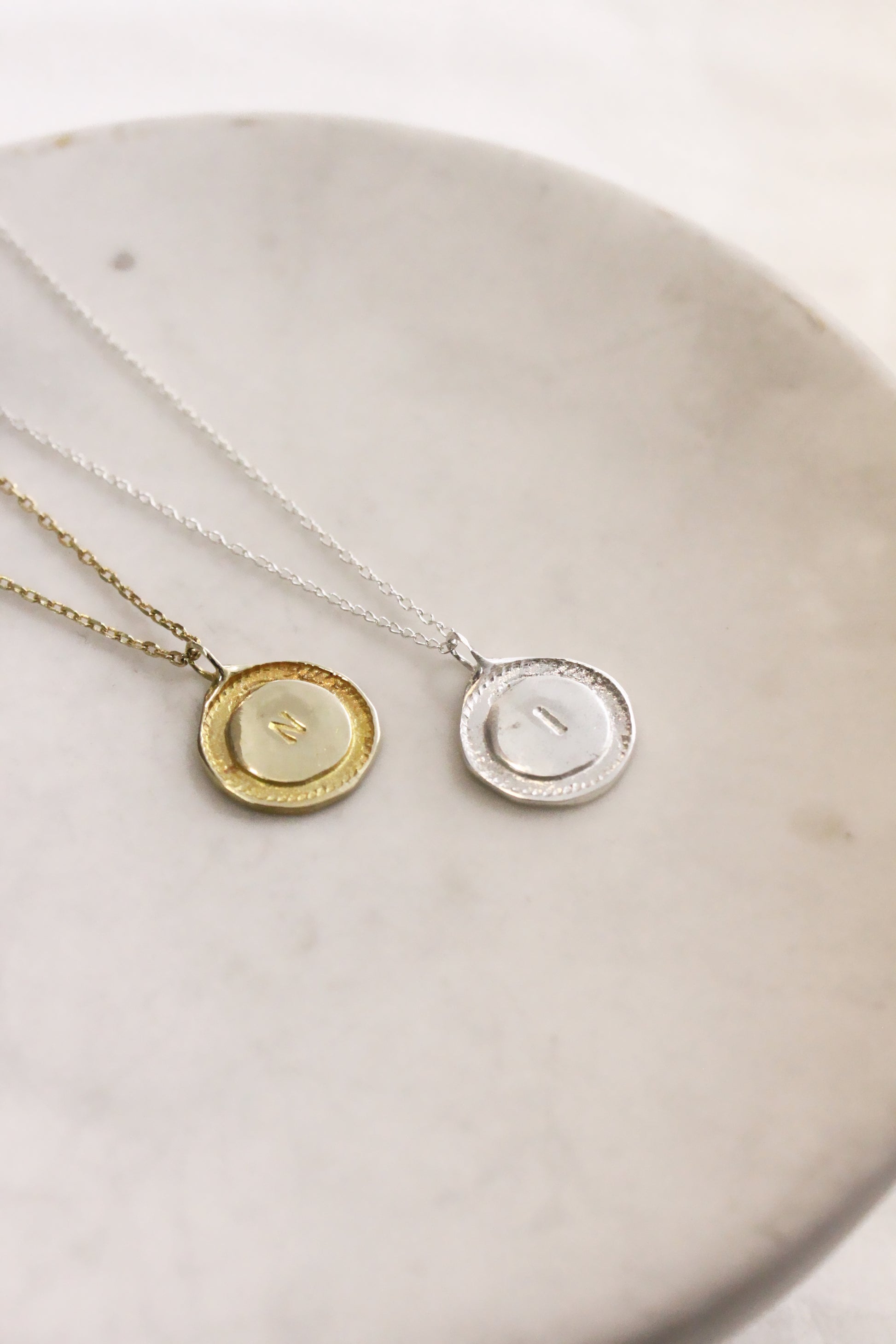 Two necklaces with circular pendants on a white dish