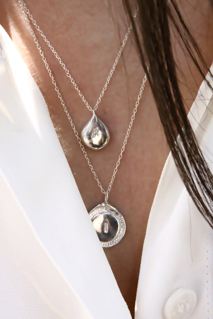 Close-up of a person wearing two silver necklaces with pendants.
