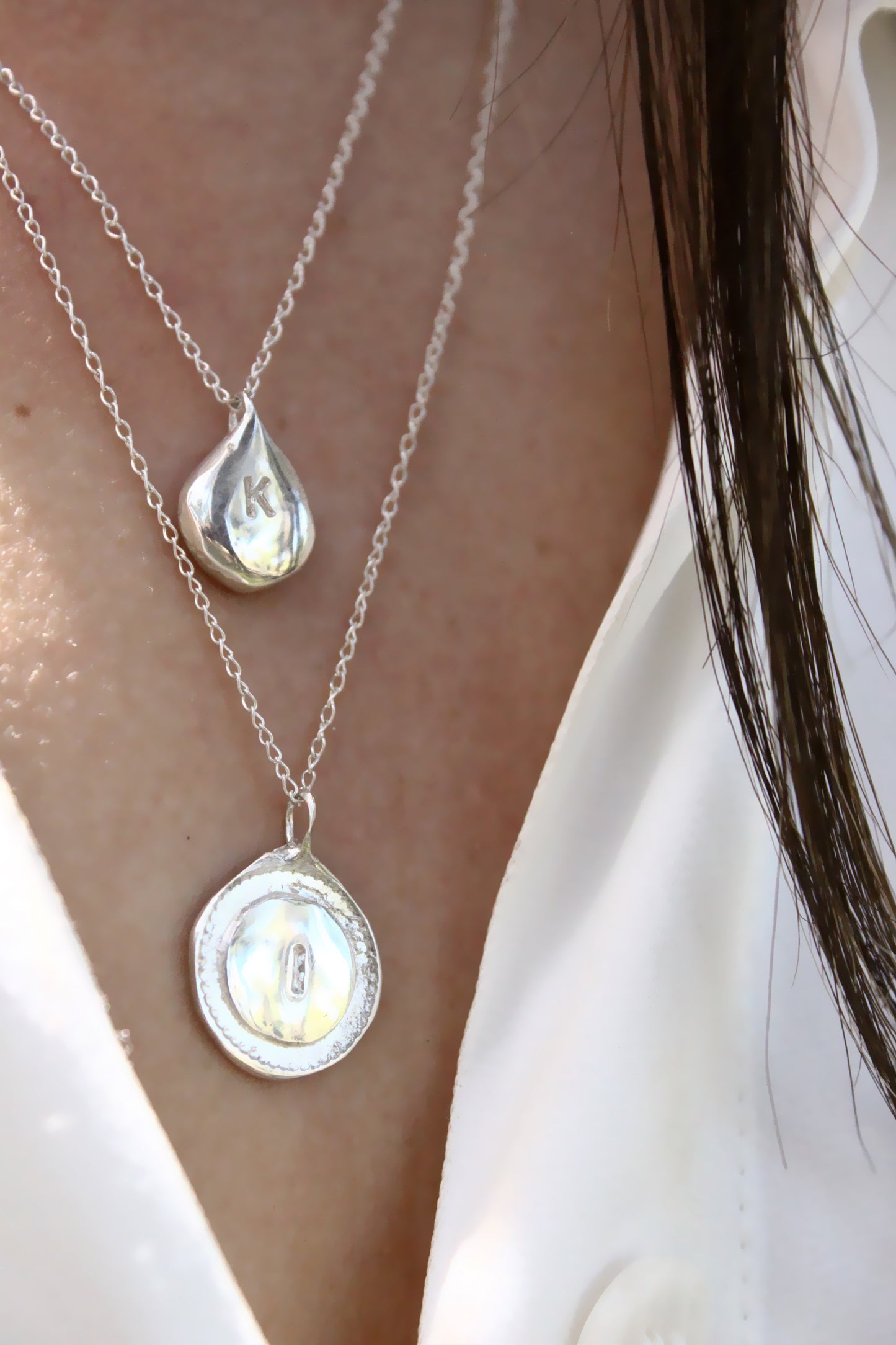 Close-up of a person wearing two silver necklaces with personalized initials monogram 