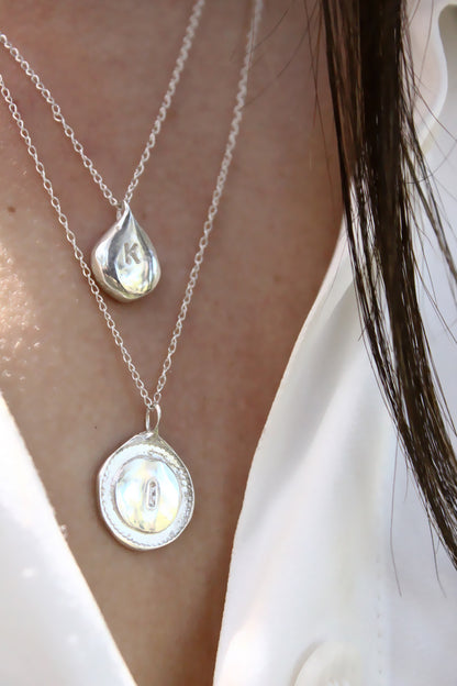 Close-up of a person wearing two silver necklaces with personalized initials monogram 