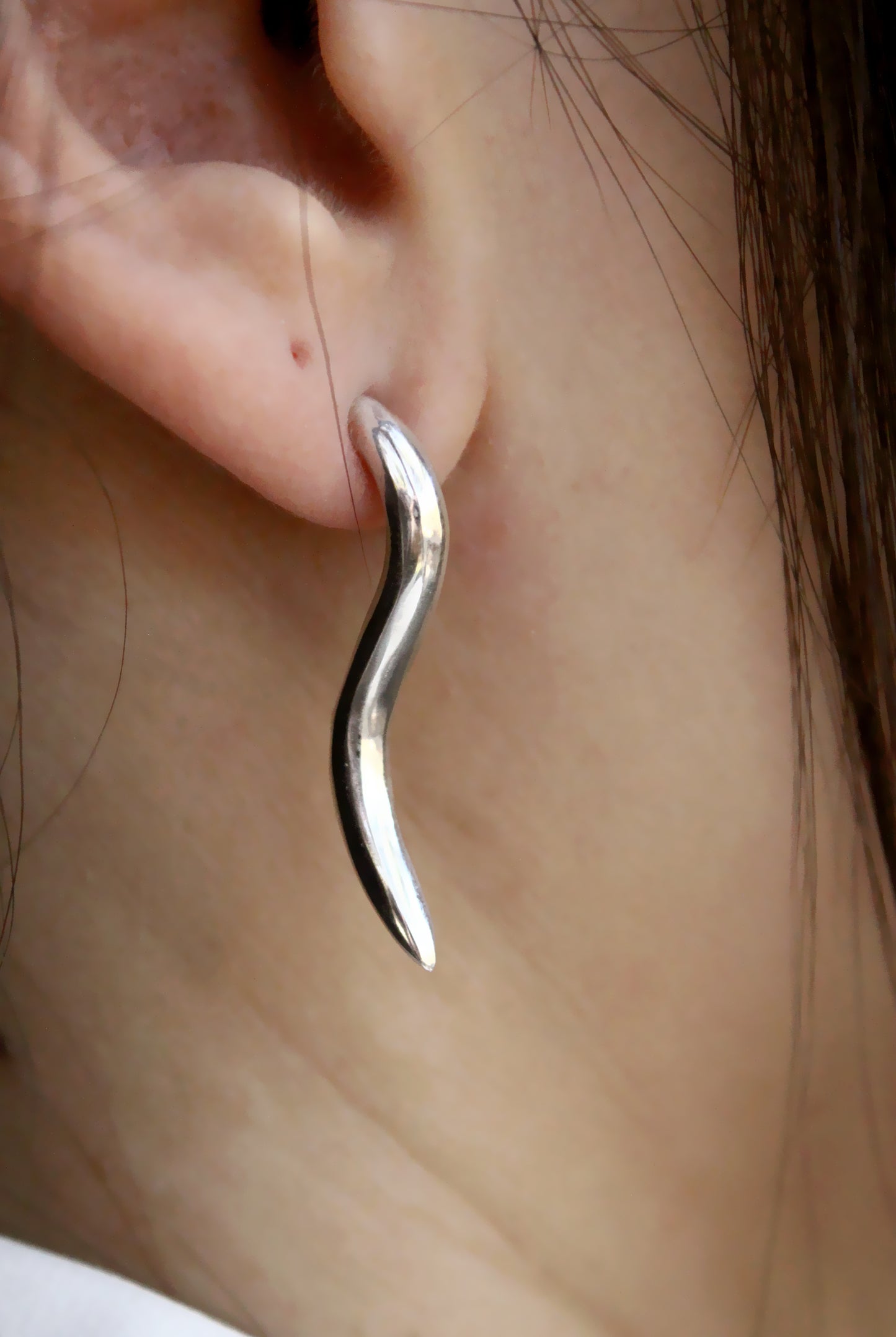 Silver wavy earring worn on a person's ear