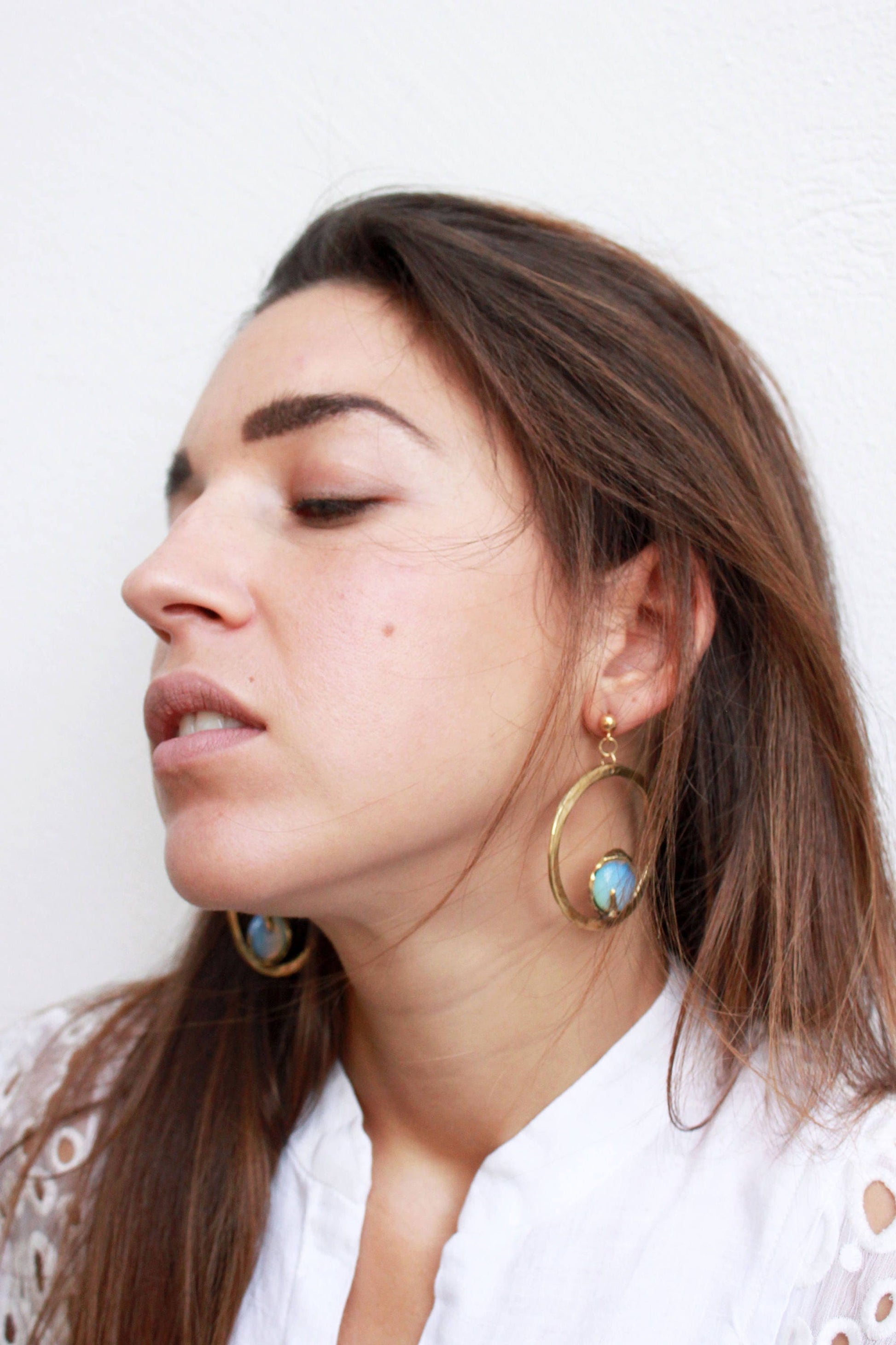 Woman wearing gold circle statement earrings with opal stones 