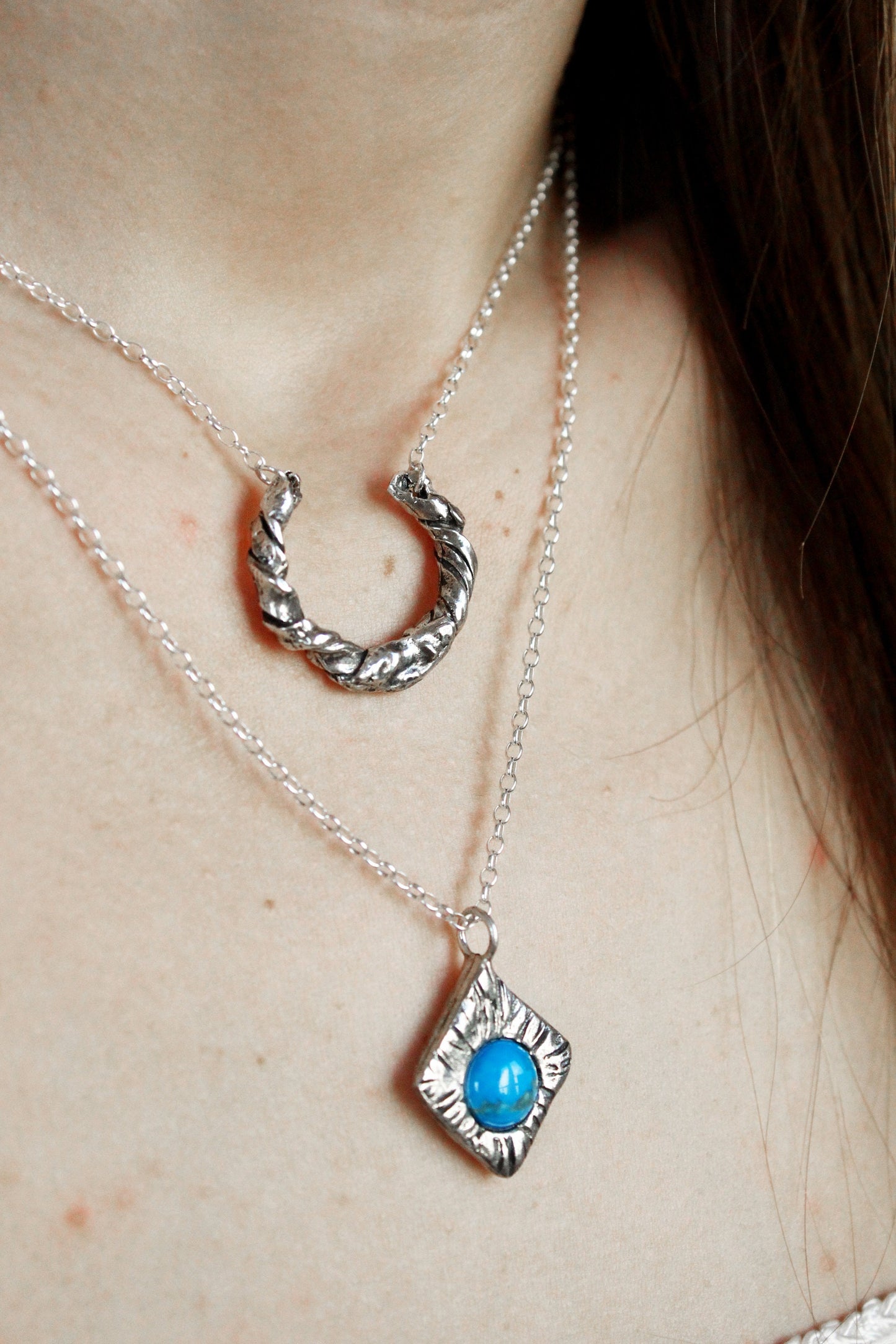 Close-up of a person wearing two silver necklaces with unique designs.
