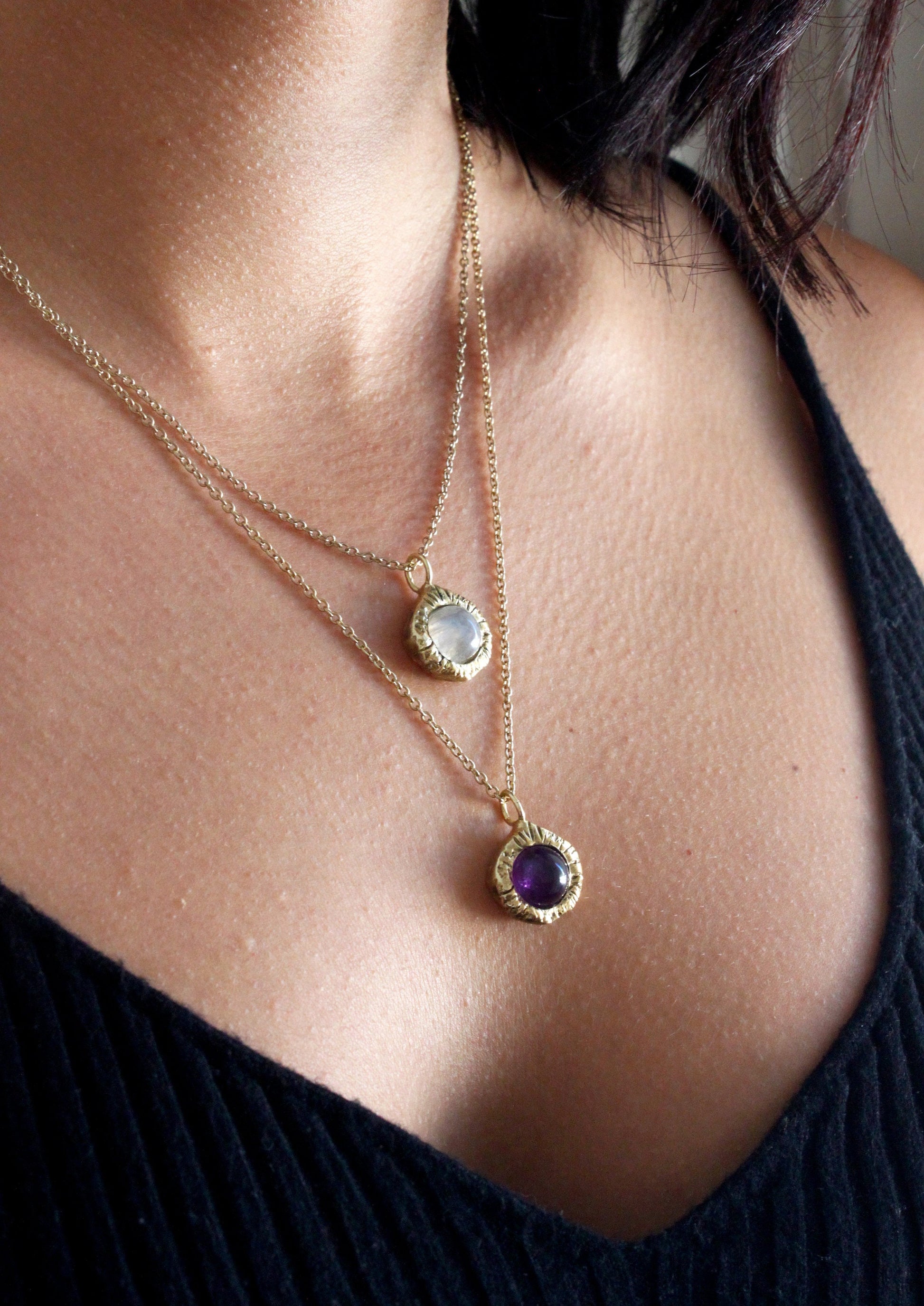 Close-up of a person wearing two gold necklaces with gemstones.