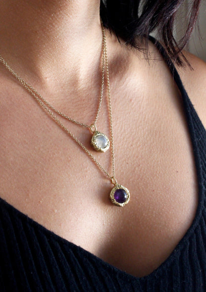 Close-up of a person wearing two gold necklaces with gemstones.