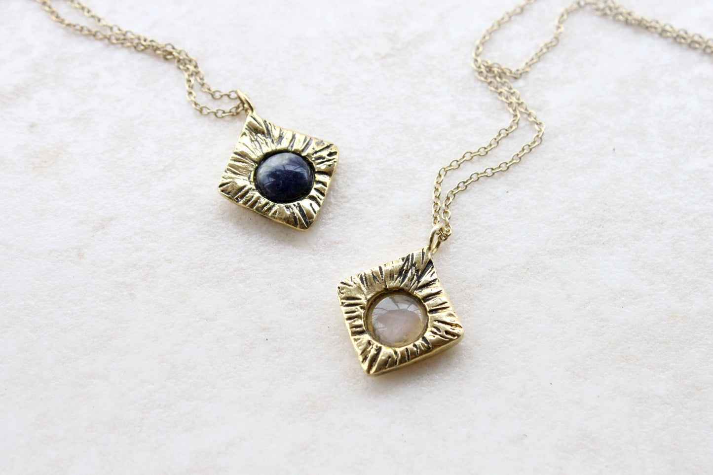 Two gold necklaces with circular pendants on a light background
