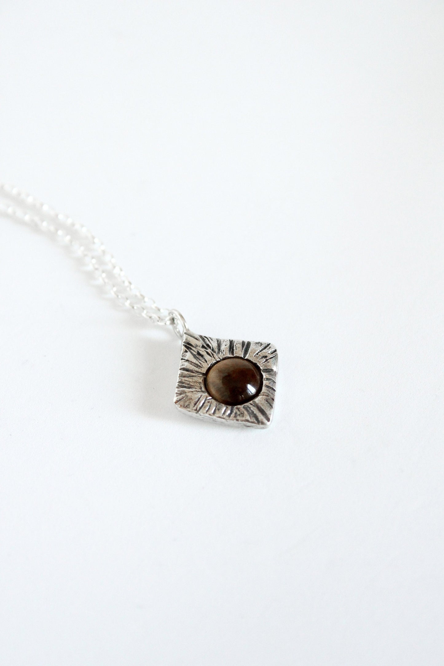 Necklace with a rhombus pendant featuring a brown stone on a white background