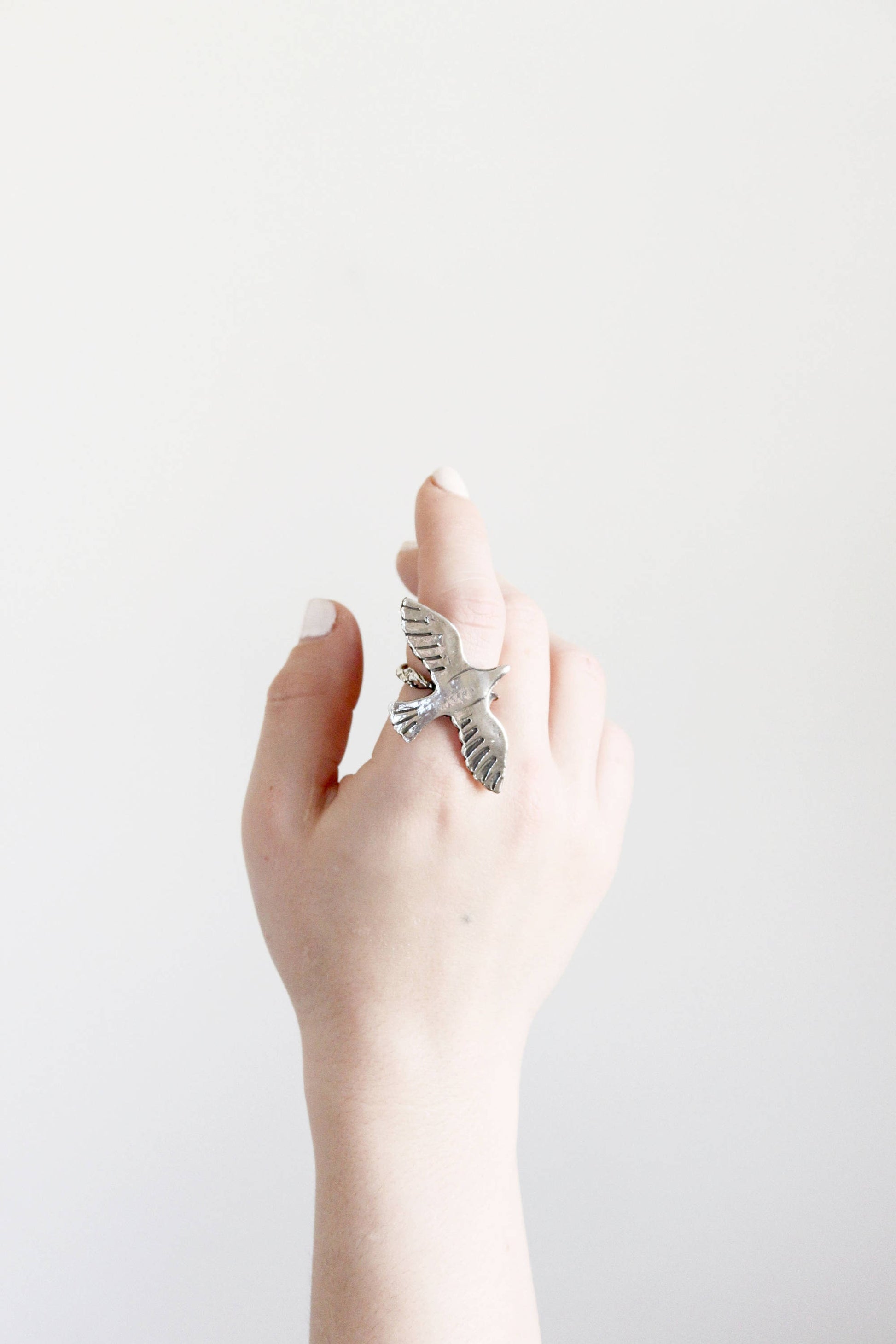 Hand wearing a silver ring with a bird design 