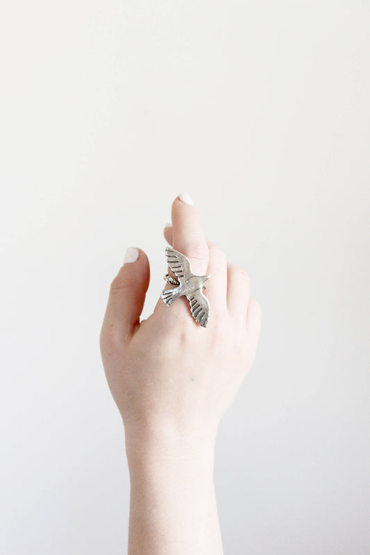 Hand wearing a silver ring with a bird design 