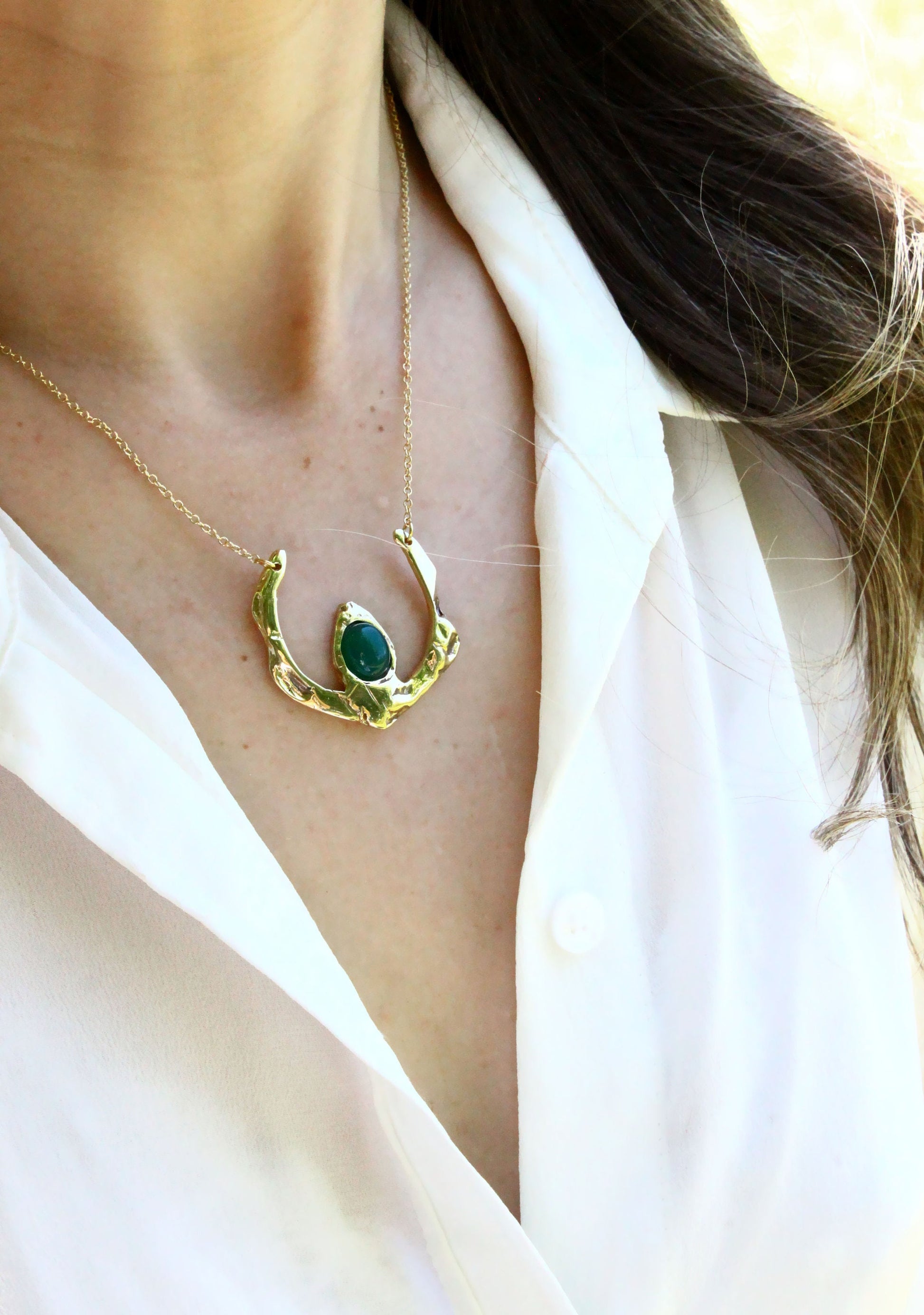 Gold necklace with a green gemstone worn by a person in a white shirt.