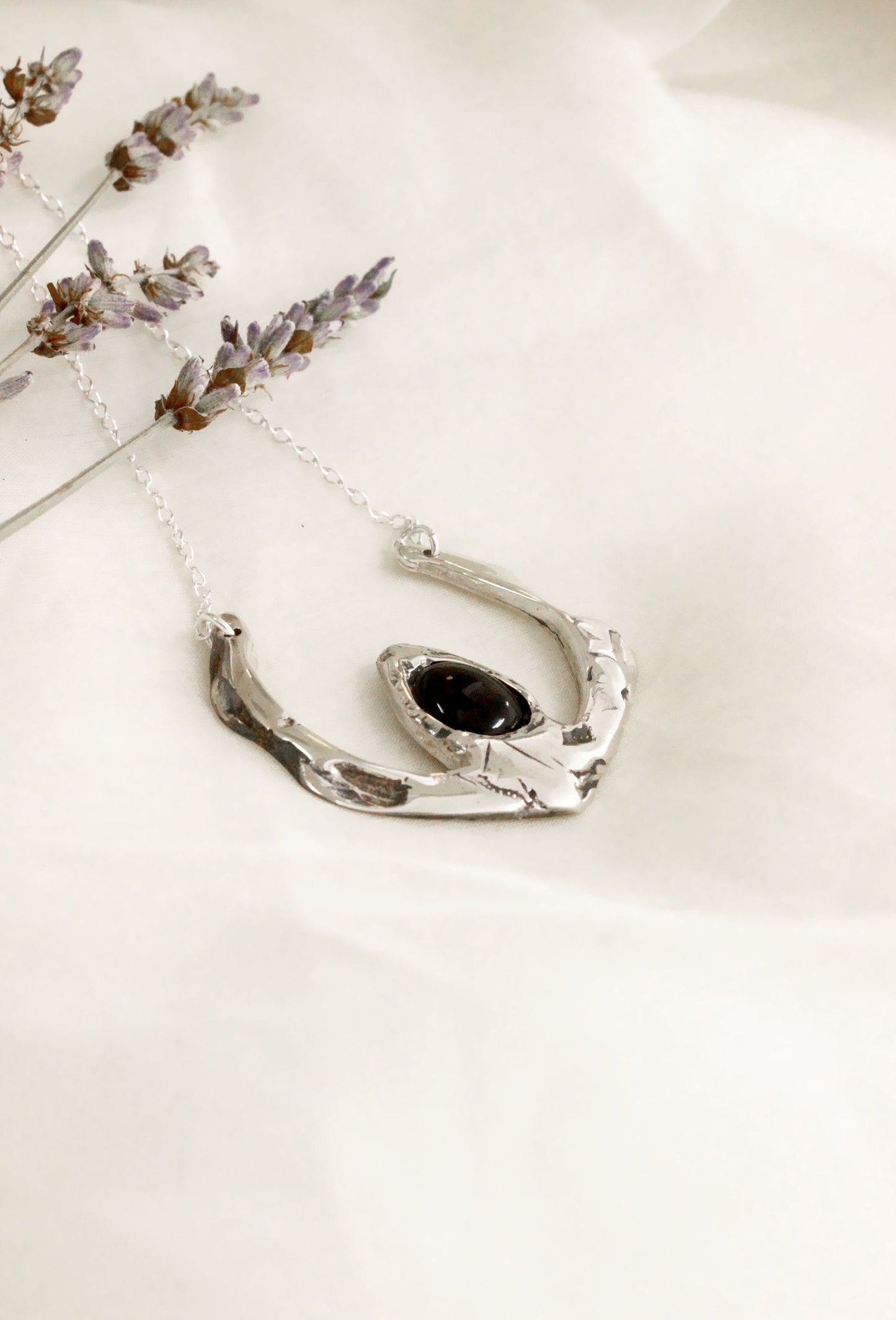 Silver necklace with a black pendant on a light background