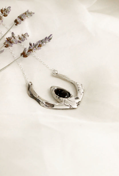 Silver necklace with a black pendant on a light background