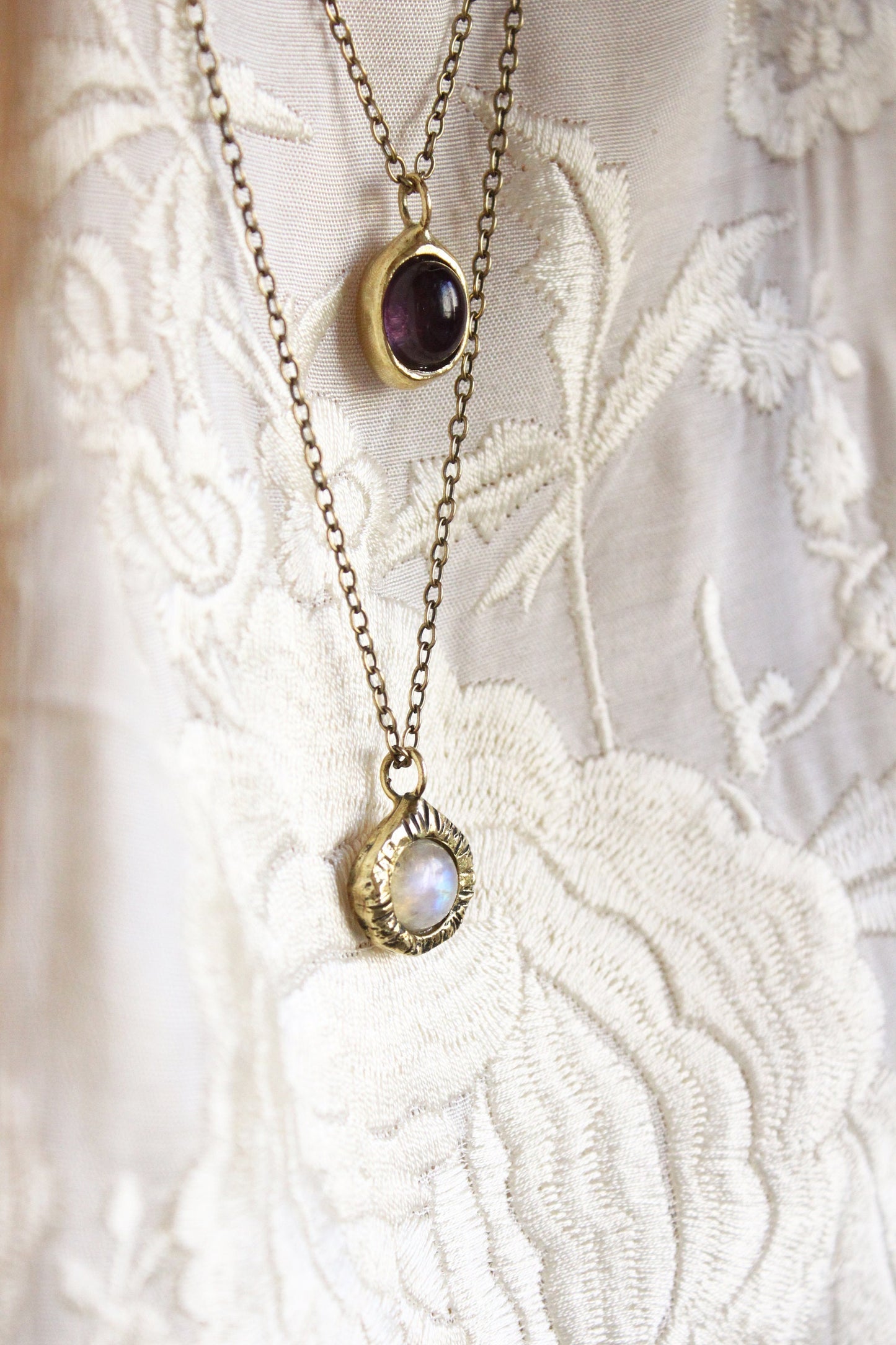 Two gold necklaces with gemstone pendants, moonstone and amethyst.
