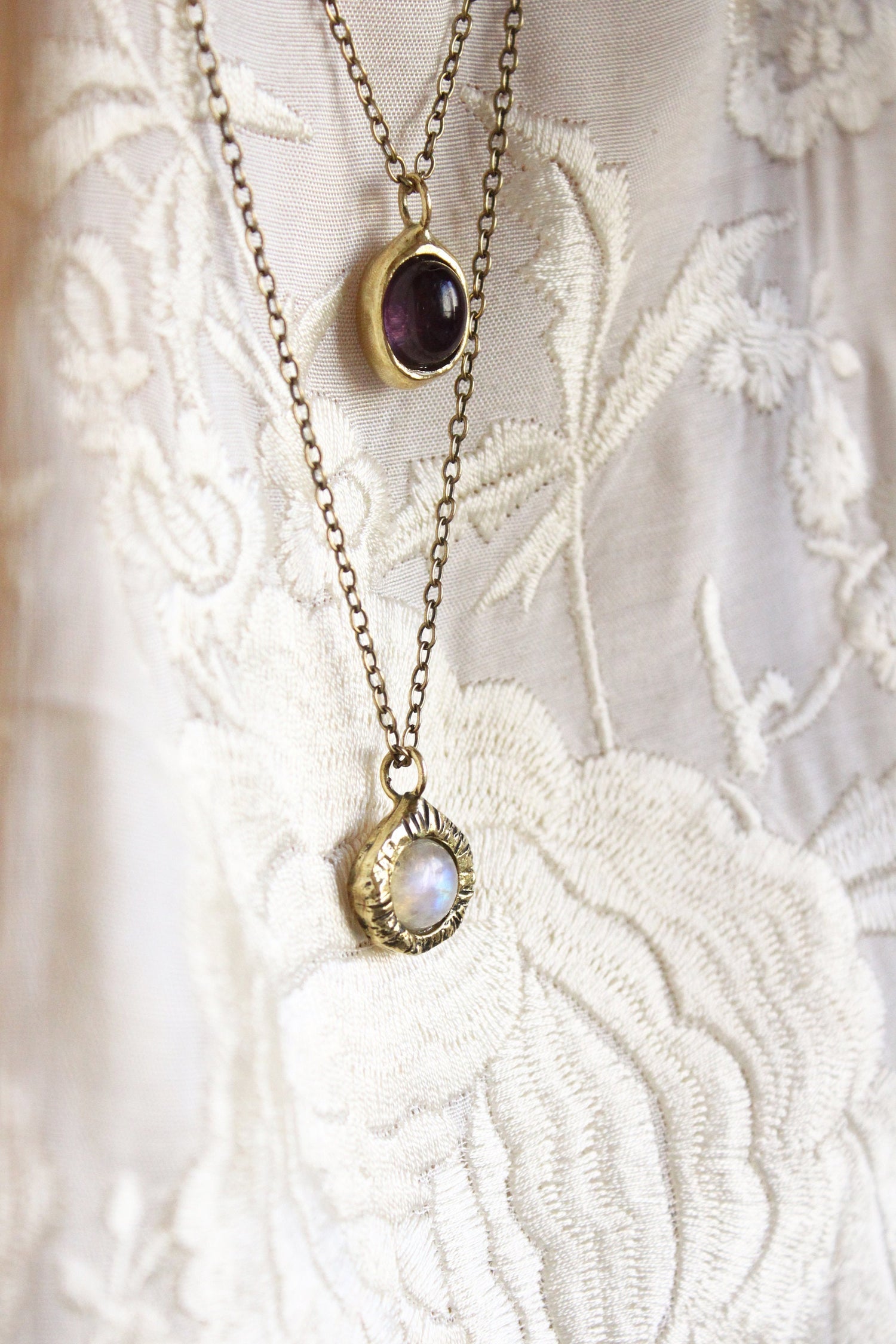 Two gold necklaces with gemstone pendants, moonstone and amethyst.