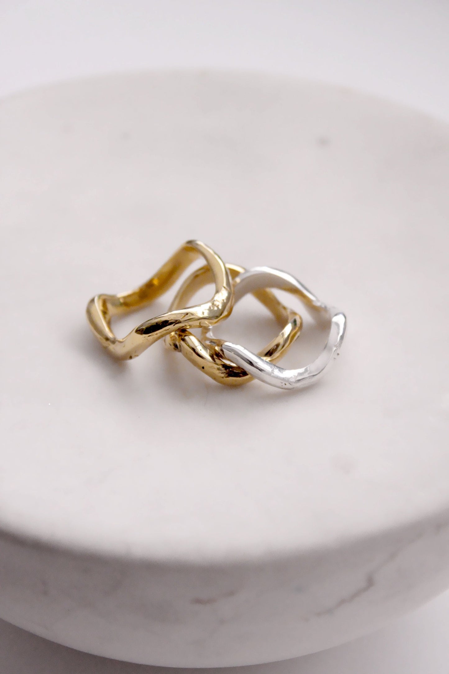 Two intertwined gold and silver rings on a white surface