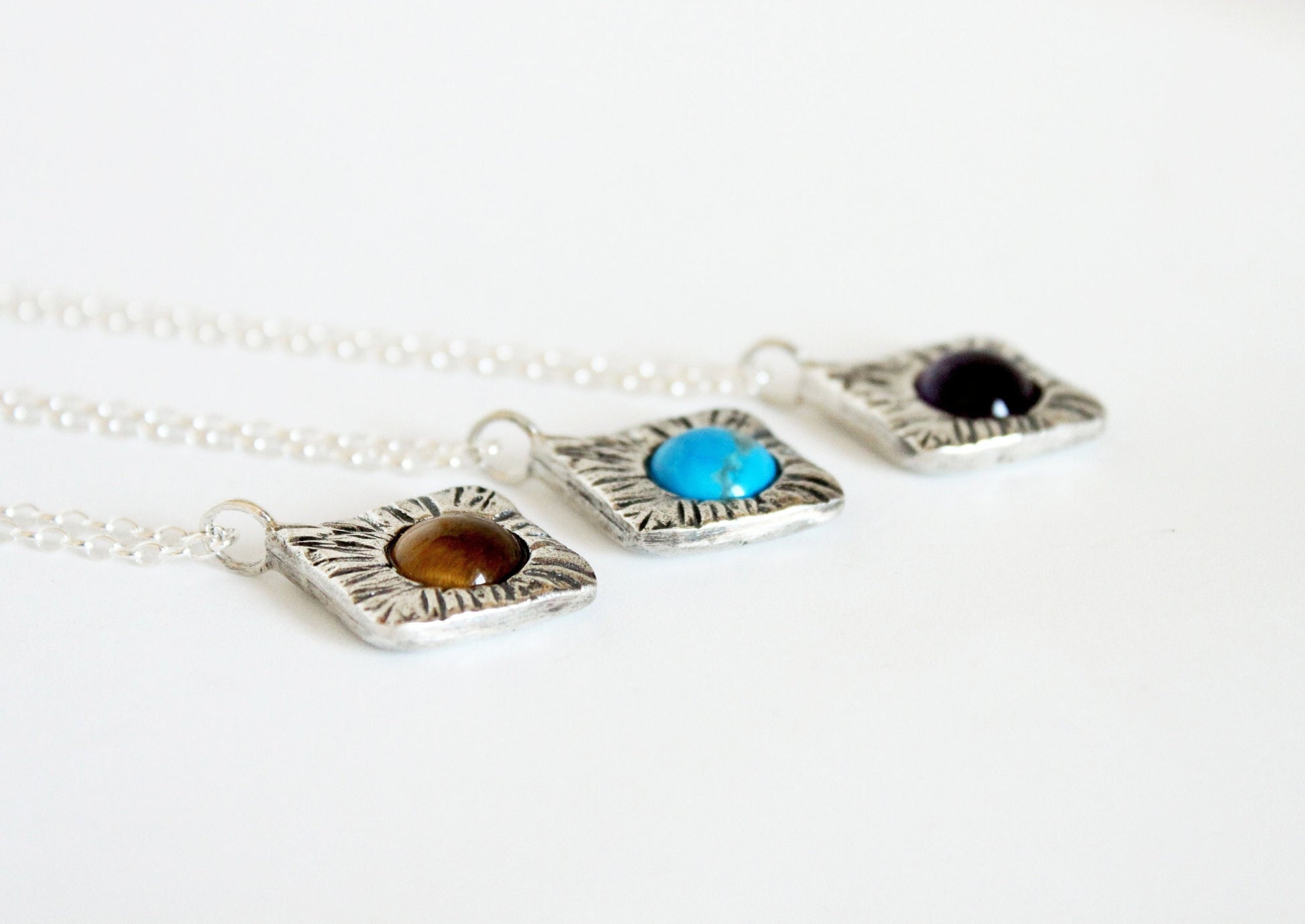 Three silver square pendants with different colored stones on a white background