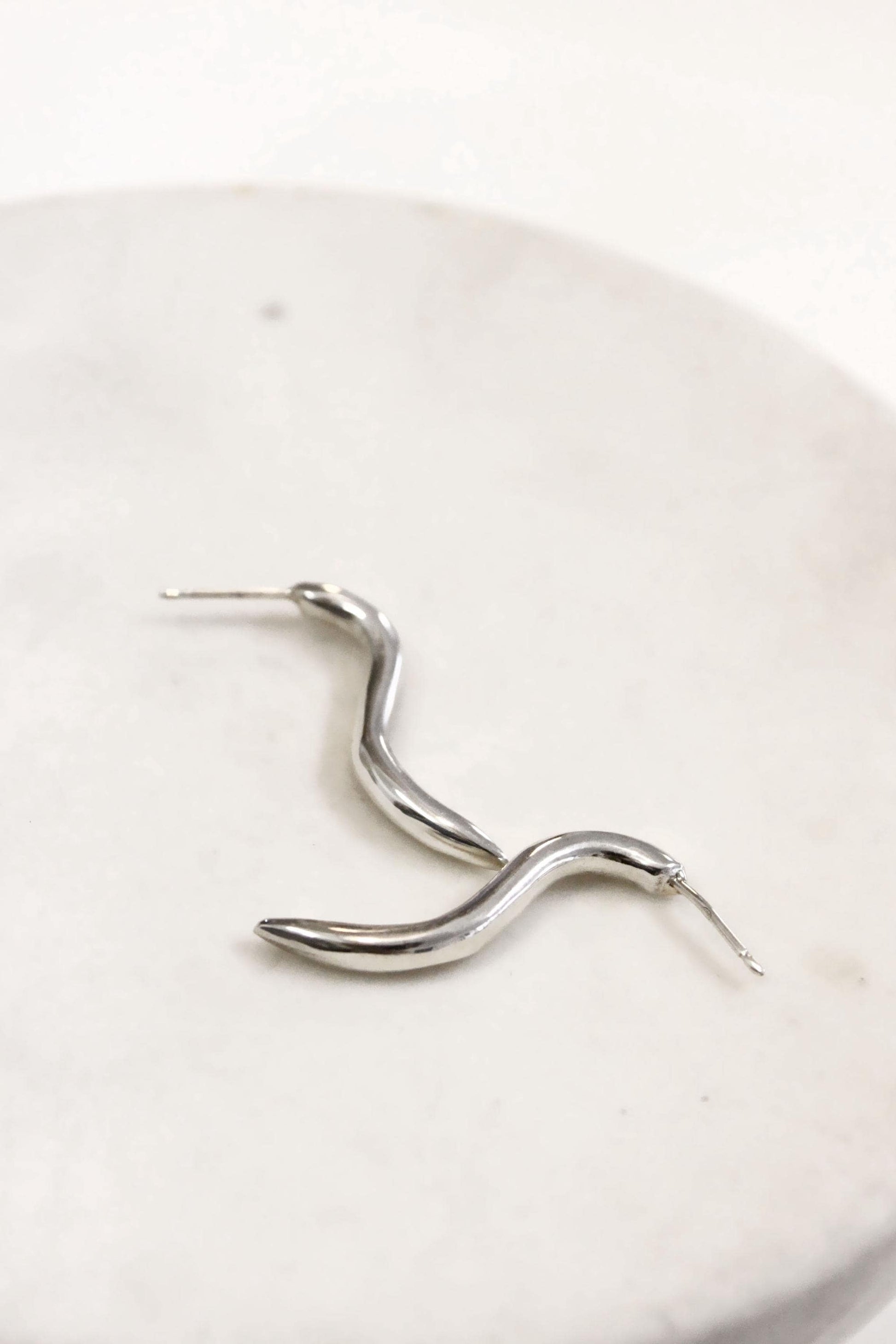 Silver wavy earring on a white plate